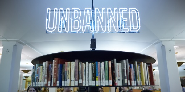 A detail view of the art installation Altar for the Unbanned, featuring a neon sign reading “Unbanned” over a shelf of books.